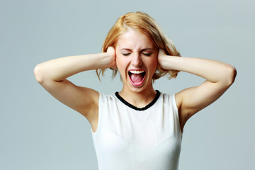 Screaming young woman with closed ears on gray background