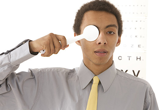 optometry concept -young man uses spoon occluder for test vision