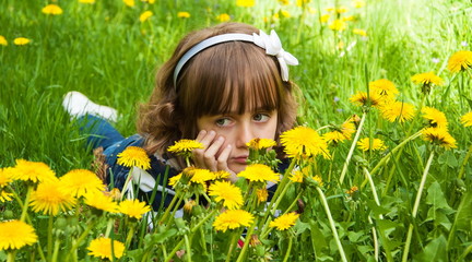 Little charming sad girl on the lawn of dandelions