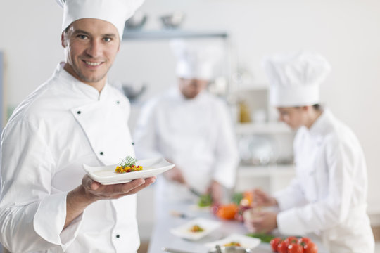 Chef Presenting A Dish With His Team In Background