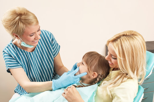 Little girl in mom's lap while dentist examines her teeth
