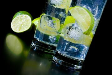 Cocktail with ice and lime slice on black table