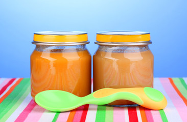 Jars of baby puree with spoon on napkin on blue background