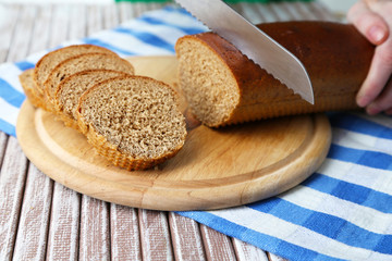 Female hands cutting bread on wooden board, close-up