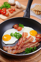 Scrambled eggs and bacon on frying pan on table close-up