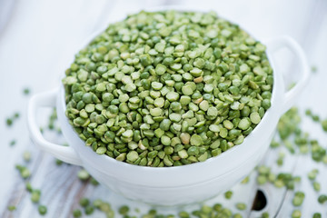 Glass bowl with split dried green peas over wooden background