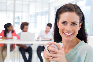 Attractive businesswoman drinking coffee with coworkers in backg