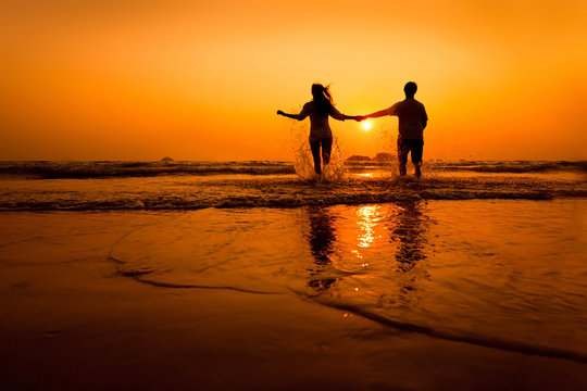 silhouettes of couple running to the sea on the beach at sunset