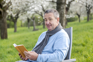 Naklejka na ściany i meble Man reading in the book under blooming cherry tree