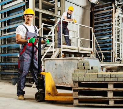 Young worker moving paving stones with pallet truck on a factory