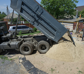 Tip truck is dumping sand in the backyard.