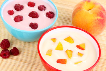 Yogurt with peaches and raspberries in bowls on bamboo mat