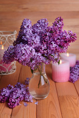 Beautiful lilac flowers in vase on table on wooden background