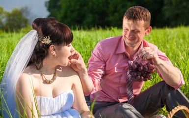 portrait of groom feeding bride with grapes at picnic