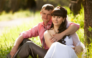 portrait of happy groom hugging bride under tree at sunny day