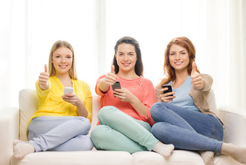 smiling teenage girls with smartphones at home