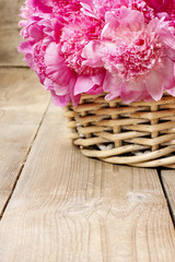 Basket of pretty pink peonies, wooden rustic background