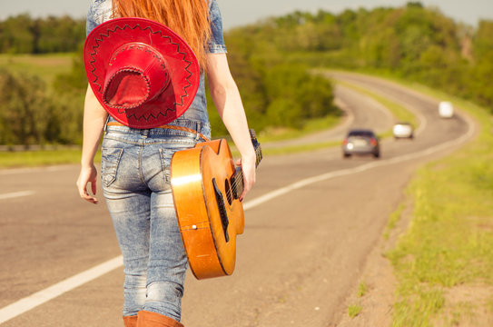 woman in jeans with guitar walking at freeway roadside