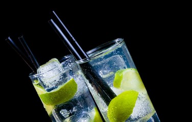 two glasses with cocktail and ice with lime slice on black