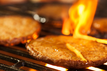 Hamburger patties on a grill with fire under