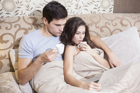 Beautiful young couple relaxing in the bed drinking coffee