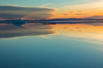 An old boat on the background of iceberg on lake in sunset.