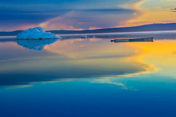 An old boat on the background of iceberg on lake in sunset. © cherniyvg