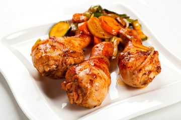 Grilled chicken legs and vegetables on white background