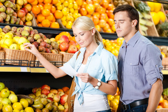 Couple with shopping list against the stacks of fruits