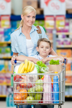 Mother and son with cart full of products in store