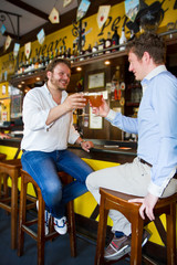 Happy man with glass of beer looking at his friend in pub 