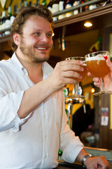 Happy man with glass of beer looking at his friend in pub 