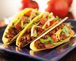 three beef tacos with cheese, lettuce and tomatos