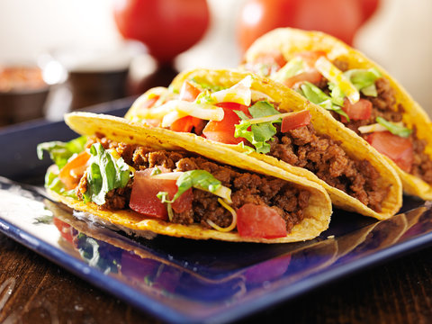 three beef tacos with cheese, lettuce and tomatos