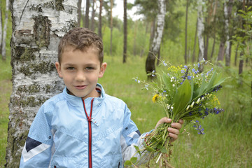 Boy standing in the woods with a bouquet of flowers.