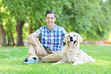 Young man relaxing in park seated with his dog