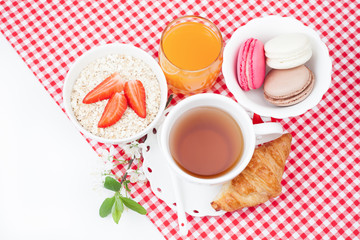 Tea cup with croissant, colourful french macaroons, oatmeal with