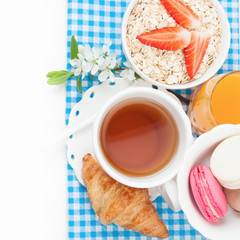 Obraz na płótnie Canvas Tea cup with croissant, colourful french macaroons, oatmeal with