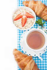 Tea cup with croissant, oatmeal with strawberries and a sprig of