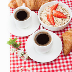 Coffee cup, oatmeal with strawberries, croissant and a sprig of