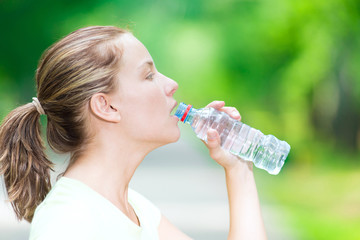 Woman drinking cold mineral water from a bottle after fitness ex