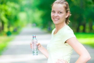 Woman drinking cold mineral water from a bottle after fitness ex