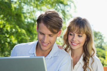 Cute couple sitting on park bench together looking at laptop