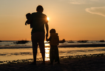 Father and two kids silhouettes on sunset beach