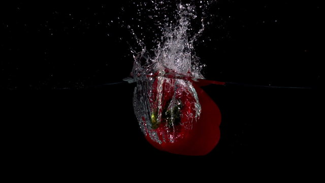 Red pepper falling in water on black background