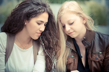 Fototapeta premium blonde and brunette beautiful stylish young women using smart ph