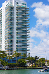 Fototapeta na wymiar Waterfront modern building with palms and white clouds