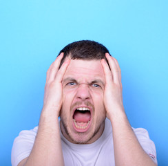 Portrait of angry man screaming and pulling hair against blue ba