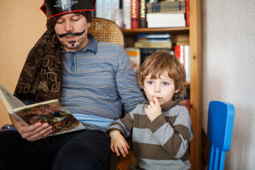 Father reading pirate book to his 4 years son, indoors