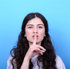 Fototapeta premium Portrait of girl with gesture for silence against blue backgroun